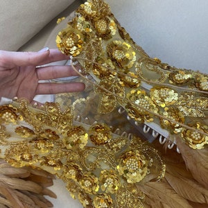 Puede incluir: Un top dorado con lentejuelas y cuentas con plumas marrones. El top est&aacute; hecho de una tela transparente y tiene un dise&ntilde;o floral.