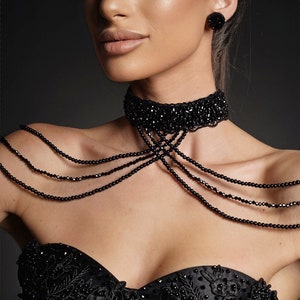 Op de afbeelding: Een vrouw draagt een zwarte strapless jurk met parelversieringen. Ze draagt een zwarte choker ketting en bijpassende oorbellen.