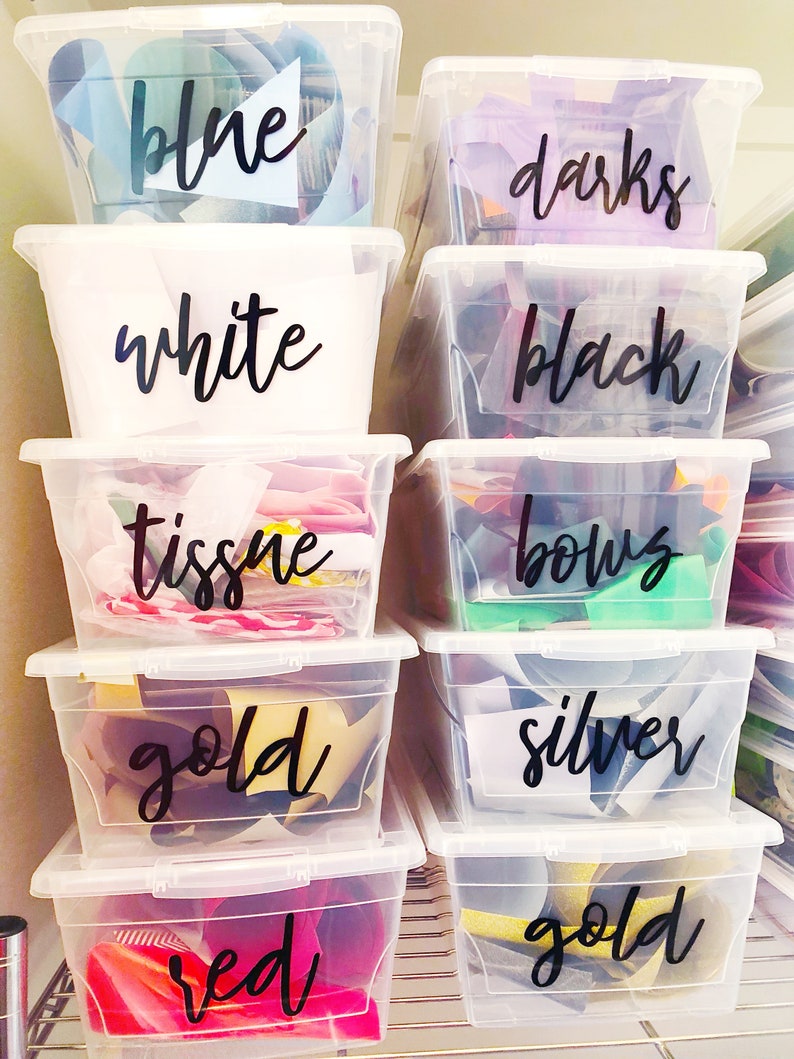May include: Clear plastic storage bins labeled with black handwritten labels. The labels read "blue", "darks", "white", "black", "tissue", "bows", "gold", "silver", "red", and "gold".