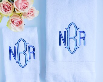 May include: Two white towels with blue embroidered monograms. The monogram is "NBR" in a script font.