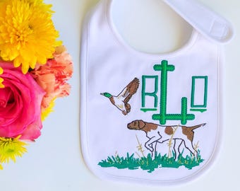 Op de afbeelding: Witte baby-slabbetje met groen geborduurd monogram "RLO" en een jachtscène met een hond en een eend.