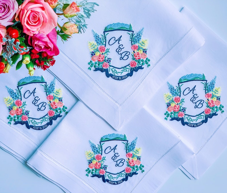May include: Four white linen napkins with embroidered floral designs and the initials "A & B" and the date "July 12, 2020".