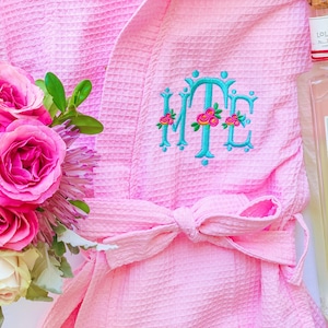 May include: A pink waffle weave robe with a blue embroidered monogram "MTE" and a bottle of "In Love with Lollia"  glass petal moisturizing bath.
