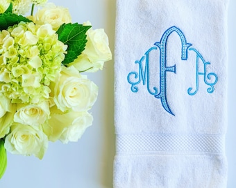 May include: White bath towel with a blue and teal embroidered monogram "MFA" in a script font.