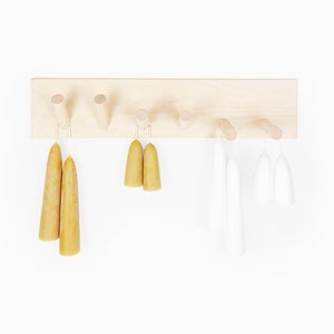 May include: A wooden wall-mounted rack with eight hooks, holding a variety of candles. The candles are in two colours: yellow and white. The rack is made of light wood and has a natural finish.