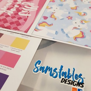 May include: A close-up of a printed design sheet with a pink and white mermaid tail with the text "Princess Party" and a blue sheet with a unicorn pattern. The sheets are on a white surface with a blue and black sticker that says "Samstables Designs" with a link to Etsy and Facebook.