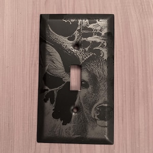 May include: Black light switch cover with an etched image of a deer in the woods.