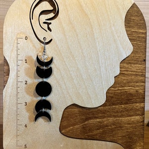 May include: Black moon phase earrings with a crystal charm hanging from a silver hook. The earrings are displayed on a wooden earring stand.
