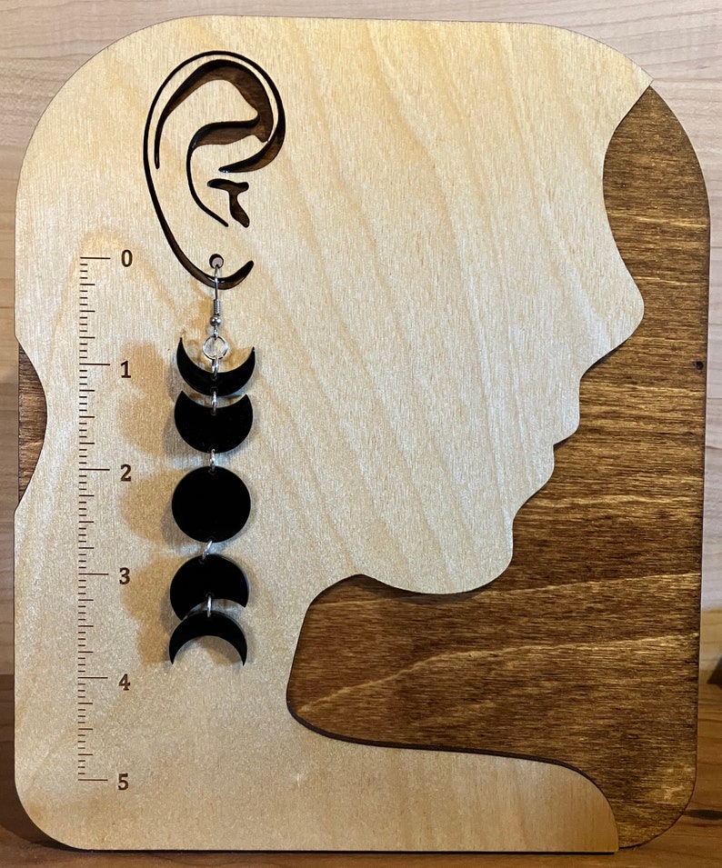 May include: Black moon phase earrings with a crystal charm hanging from a silver hook. The earrings are displayed on a wooden earring stand.