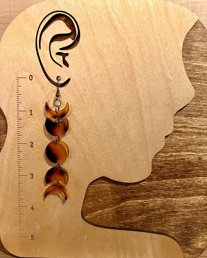 May include: A pair of brown and gold moon phase earrings. The earrings are made of resin and have a dangling design. The earrings are about 4 inches long.