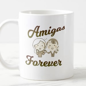 Może przedstawiać: Biały ceramiczny kubek z napisem "Amigas Forever" w złotym skrypcie. Kubek przedstawia kresk&oacute;wkową ilustrację dw&oacute;ch uśmiechniętych postaci. Kubek ma zakrzywiony uchwyt i nadaje się do gorących lub zimnych napoj&oacute;w.