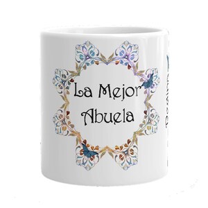 May include: White ceramic mug with a decorative floral design in blue, gold, and purple. The mug features the text "La Mejor Abuela" in black script, surrounded by a floral wreath. A perfect gift for a grandmother.