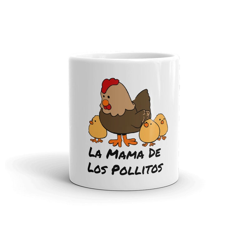 May include: White ceramic mug featuring a cartoon hen with three chicks. The hen is brown with a red comb, and the chicks are yellow. The text "LA MAMA DE LOS POLLITOS" is printed in black.