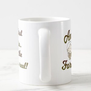 Może przedstawiać: Biały ceramiczny kubek do kawy z zakrzywionym uchwytem. Kubek ma złoty napis &bdquo;I pierwszy, kt&oacute;ry... zobaczy prawdziwe!&rdquo; oraz rysunkową ilustrację kobiety.