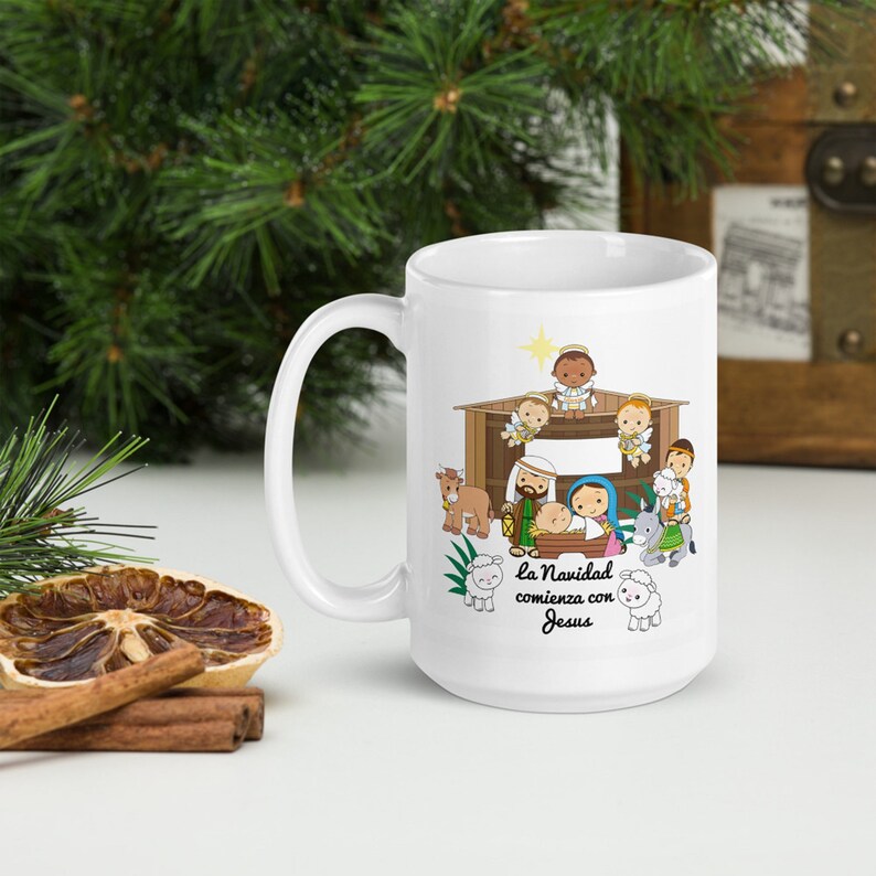 May include: White ceramic mug featuring a nativity scene illustration. The design includes a stable, baby Jesus, Mary, Joseph, angels, and animals. Text in Spanish reads "la Navidad comienza con Jesus".