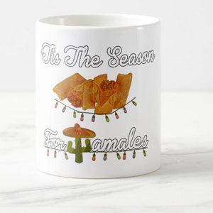 以下が含まれることがあります： 「Tis The Season For Tamales」の文字が入った白いセラミックマグ。マグには、タマレス、ソンブレロ、サボテンのグラフィックが描かれており、すべてストリングライトで飾られています。
