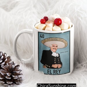 May include: White ceramic mug featuring a portrait of a man in a charro suit, with the text "El Rey". The mug is filled with marshmallows and red berries. The website ChicaSunshine.com is printed at the bottom.