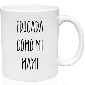 May include: White ceramic mug with the text "EDUCADA COMO MI MAMI" in black, a Spanish phrase. The mug has a curved handle and a cylindrical shape, suitable for hot or cold beverages. A simple, everyday item.