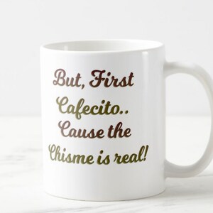 Może przedstawiać: Biały ceramiczny kubek z napisem "But, First Cafecito.. Cause the Chisme is real!" w brązowo-złotych literach. Kubek ma zakrzywiony uchwyt.