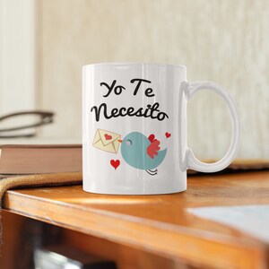 May include: White ceramic mug with the Spanish text "Yo Te Necesito" in black script. A blue bird with a red wing and a letter graphic is printed on the mug, along with red heart accents.