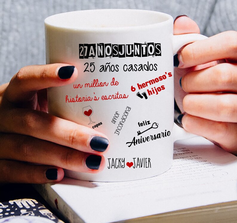 Puede incluir: Taza de cer&aacute;mica blanca con texto negro y rojo, sostenida por una persona. La taza presenta frases como "27 a&ntilde;os juntos", "25 a&ntilde;os casados" y "Feliz Aniversario". El texto adicional incluye "Jacky & Javier" con un s&iacute;mbolo de coraz&oacute;n.