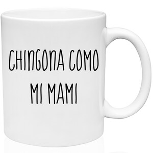 May include: White ceramic mug with the text "CHINGONA COMO MI MAMI" in black, handwritten-style lettering. The mug has a standard handle and a glossy finish. A simple, everyday coffee or tea mug.