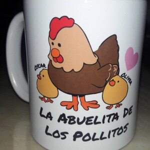 May include: White ceramic mug featuring a cartoon hen with two chicks and a pink heart. The hen is brown, tan, and red, with the text "LA ABUELITA DE LOS POLLITOS" below the image. The chicks are yellow, and the names "OSCAR" and "OLIVER" are written on the mug.