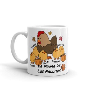 May include: White ceramic mug with a cartoon hen and six chicks, pumpkins, and autumn leaves. The text "LA MAMA DE LOS POLLITOS" is printed below the chicks. The hen is brown with a red comb.