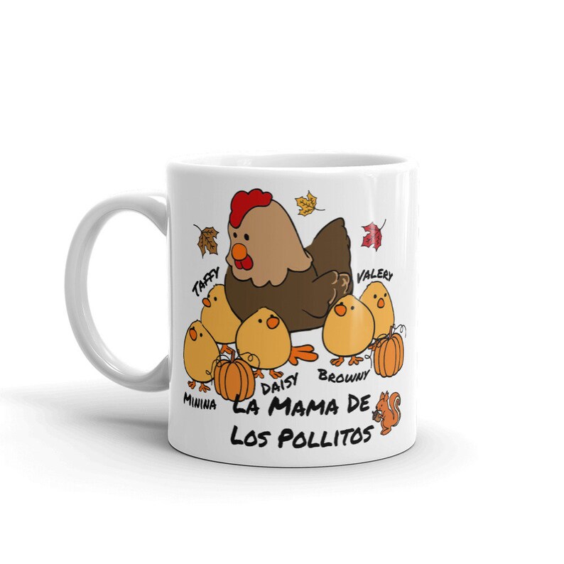 May include: White ceramic mug with a cartoon hen and six chicks, pumpkins, and autumn leaves. The text "LA MAMA DE LOS POLLITOS" is printed below the chicks. The hen is brown with a red comb.