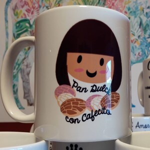 May include: White ceramic mug featuring a cartoon girl with brown hair and a smiling face. The mug has the text "Pan Dulce con Cafecito" and illustrations of sweet bread. A handle is on the left side of the mug.