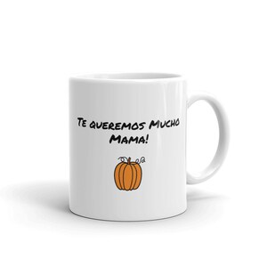 May include: White ceramic mug with a black handwritten message "Te queremos mucho Mama!" and a cartoon orange pumpkin illustration. The mug has a curved handle and is suitable for hot or cold drinks.