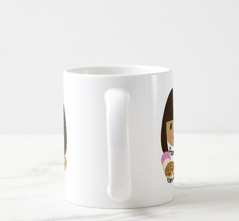 May include: White ceramic mug featuring a cartoon illustration of a person holding a concha pastry. The text "Pan con concha" is written on the mug in black script. The illustration has brown hair and a pink and brown pastry.