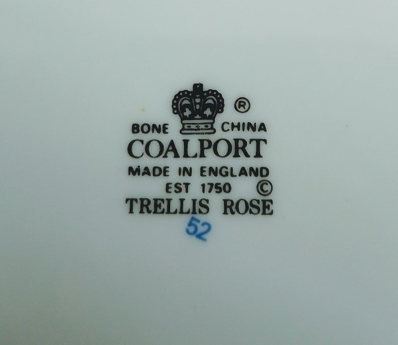 May include: A white porcelain plate with a black and white Coalport Trellis Rose china mark. The mark includes a crown, the words "Bone China", "Coalport", "Made in England", "Est 1750", and "Trellis Rose". The number "52" is written in blue ink.