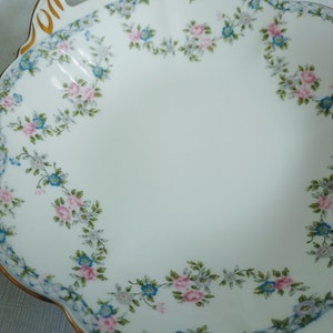 May include: A white porcelain serving dish with a scalloped edge and gold trim. The dish is decorated with a floral pattern of pink and blue flowers.