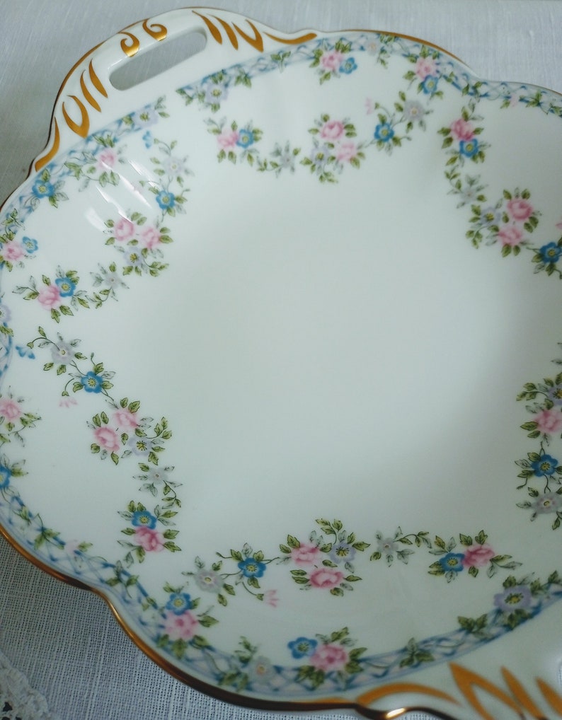 May include: A white porcelain serving dish with a scalloped edge and gold trim. The dish is decorated with a floral pattern of pink and blue flowers.