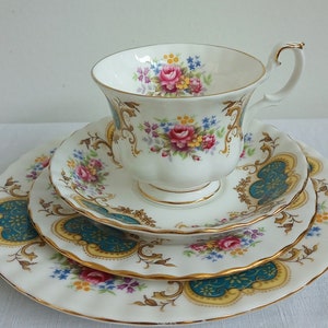 Peut inclure: Un ensemble de tasse et soucoupe en porcelaine blanche avec un motif floral et une bordure dorée. L'ensemble présente un motif floral délicat avec des fleurs roses, jaunes et bleues. La soucoupe a un bord festonné et un motif bleu sarcelle et or.