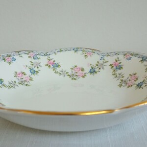 May include: A white porcelain serving dish with a scalloped edge and two handles. The dish is decorated with a floral pattern of pink and blue flowers on a white background. The rim of the dish is trimmed with a gold band.