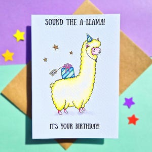 Puede incluir: Una tarjeta de cumplea&ntilde;os con una llama de dibujos animados que lleva un sombrero de fiesta y lleva un regalo. La tarjeta dice "Sound the A-llama! It's your birthday!"