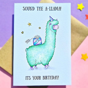Puede incluir: Una tarjeta de cumplea&ntilde;os con un dibujo de una llama de dibujos animados que lleva un gorro de fiesta y lleva un regalo. La tarjeta tiene un fondo azul con estrellas doradas y el texto "SOUND THE A-LLAMA! ITS YOUR BIRTHDAY!"