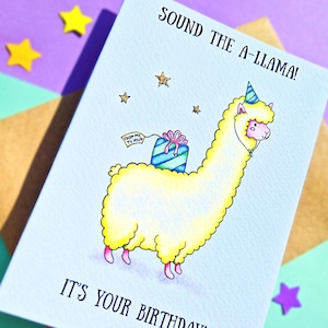 Puede incluir: Una tarjeta de cumplea&ntilde;os azul claro con una llama de dibujos animados que lleva un sombrero de fiesta y lleva un regalo. La tarjeta dice "Sound the A-llama! It's your birthday!"