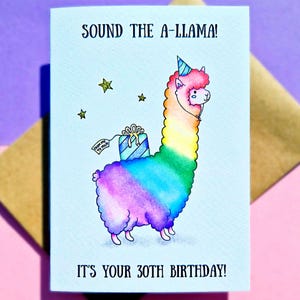 Puede incluir: Una tarjeta de cumplea&ntilde;os con un lama de dibujos animados que lleva un gorro de fiesta y lleva un regalo. El lama es de color arco&iacute;ris y la tarjeta dice "Sound the A-Llama! It's your 30th Birthday!"