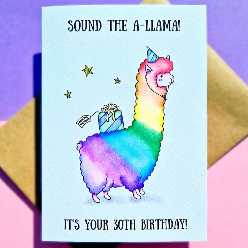 Puede incluir: Una tarjeta de cumplea&ntilde;os con un lama de dibujos animados que lleva un gorro de fiesta y lleva un regalo. El lama es de color arco&iacute;ris y la tarjeta dice "Sound the A-Llama! It's your 30th Birthday!"
