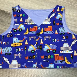 May include: Blue vest with construction vehicle print. Features trucks, excavators, and traffic cones. The vest has the words "WORK", "DIG", and "GO" printed on it. It has three black buttons.