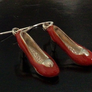 May include: A pair of red shoe-shaped earrings with silver hooks. The shoes have a silver detail on the toe.