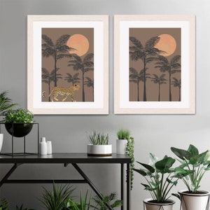 May include: Two framed prints with a brown background and black palm trees. The print on the left features a leopard walking through the trees. The print on the right features a large orange sun.