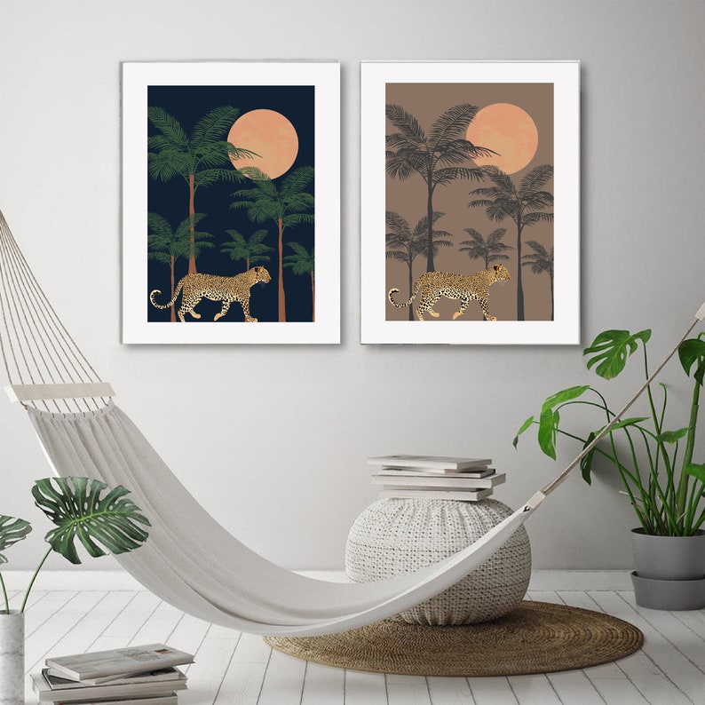 May include: Two framed prints with a jungle scene. Each print features a leopard walking through a palm tree forest under a large, orange moon. One print has a dark blue background and the other has a light brown background.