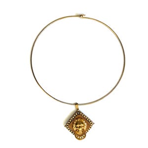 May include: Gold-toned choker necklace with a lion's head pendant. The pendant is square-shaped with a textured wooden background and a gold lion's head with a ring in its mouth. The necklace has a simple, thin, circular design.