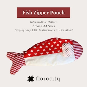 Może przedstawiać: Ręcznie robiona saszetka z zamkiem błyskawicznym w kształcie ryby. Góra jest czerwona z białymi sercami, brzuch jest biały, a ogon jest w czerwoną i białą kratę. Tekst "Fish Zipper Pouch" i "florocity" są dołączone.