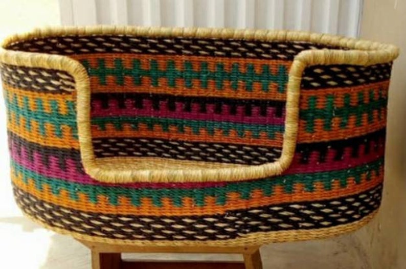 May include: A woven pet bed with a colorful geometric pattern in shades of orange, green, purple, and black. The bed has a thick, woven rim and a raised edge.