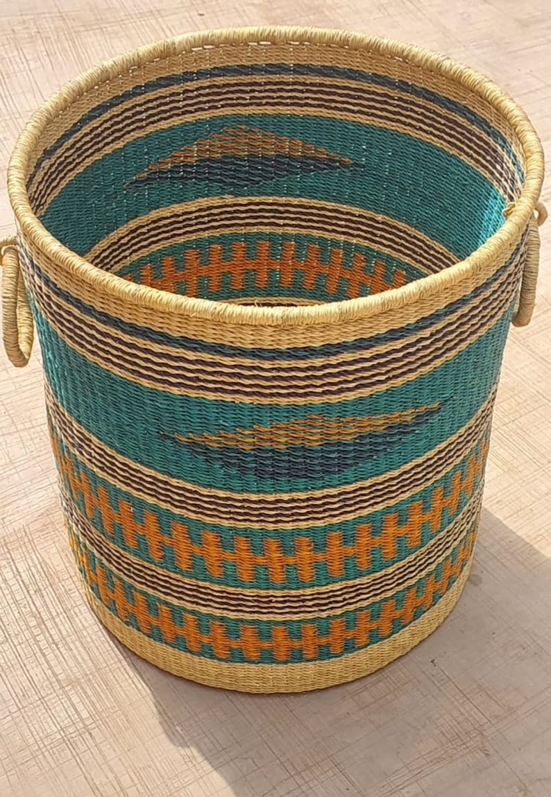 Op de afbeelding: Een geweven opbergmand met een gestreept patroon in turquoise, bruin en oranje. De mand heeft twee handvatten en is gemaakt van natuurlijke materialen.